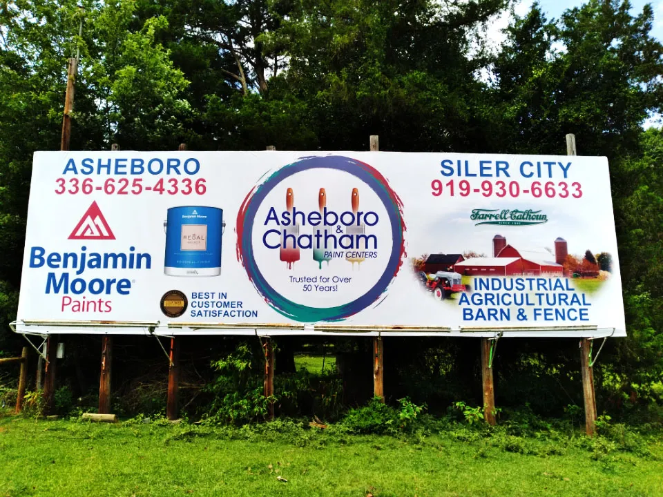 Roadside billboard for Asheboro and Chatham Paint Centers featuring Benjamin Moore branding, set against green trees.