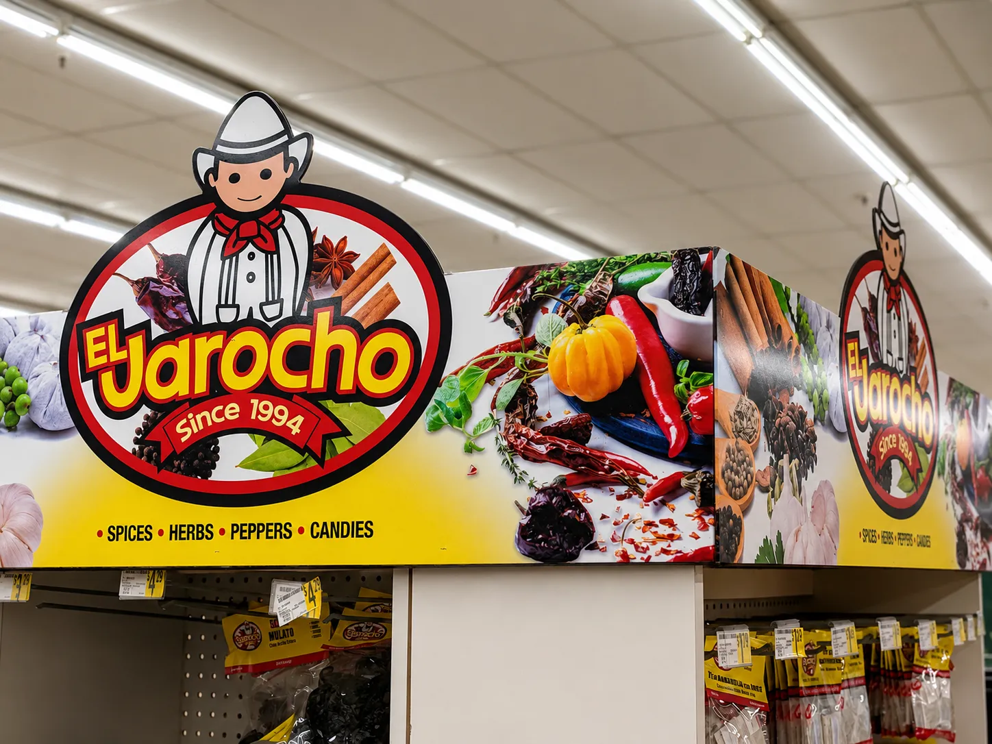 Large El Jarocho aisle signage in a grocery store with the brand's mascot logo, 'Since 1994,' and vivid photos of peppers and spices.