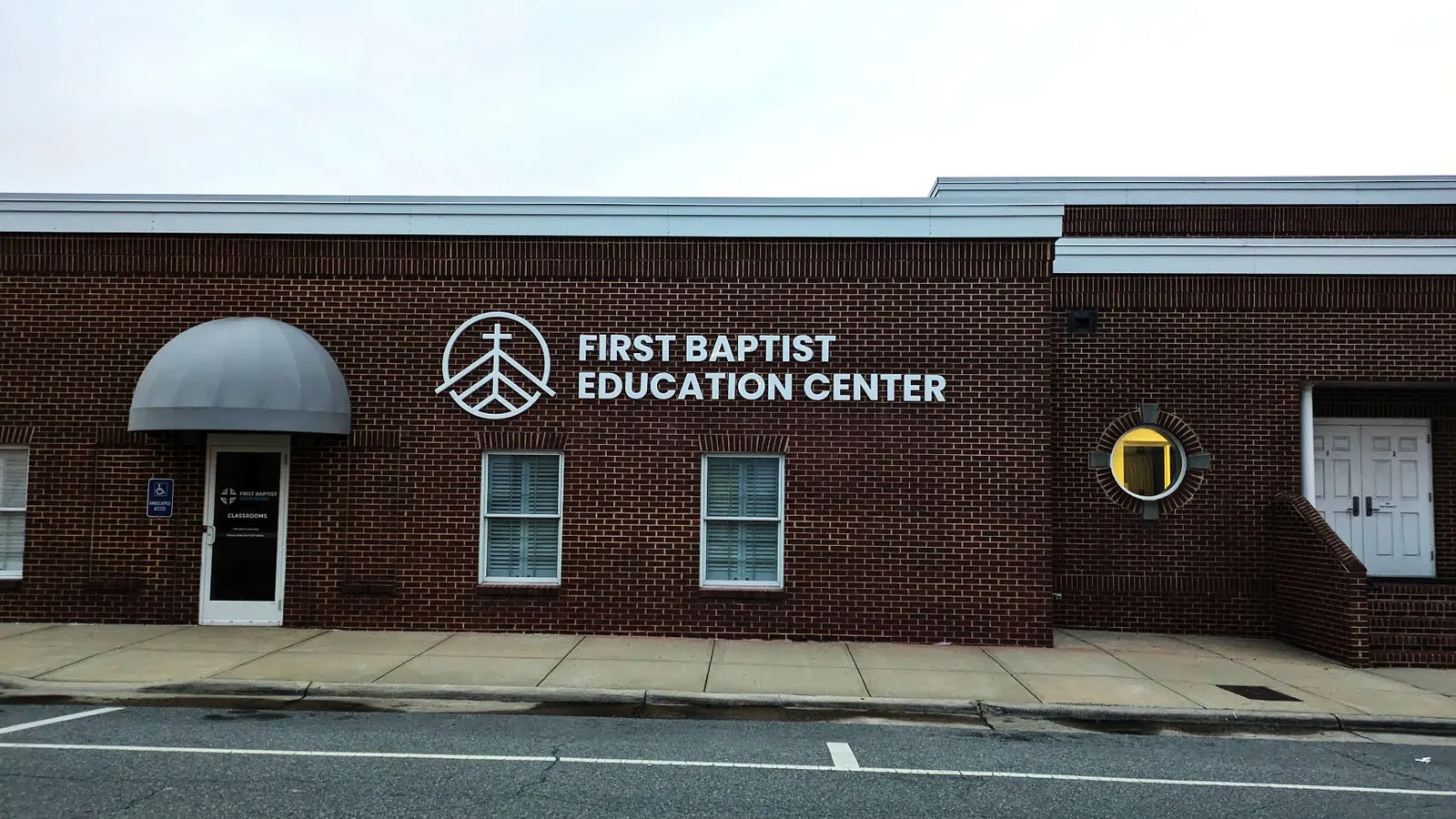 White dimensional letters and logo reading First Baptist Education Center installed on a dark brick building wall.