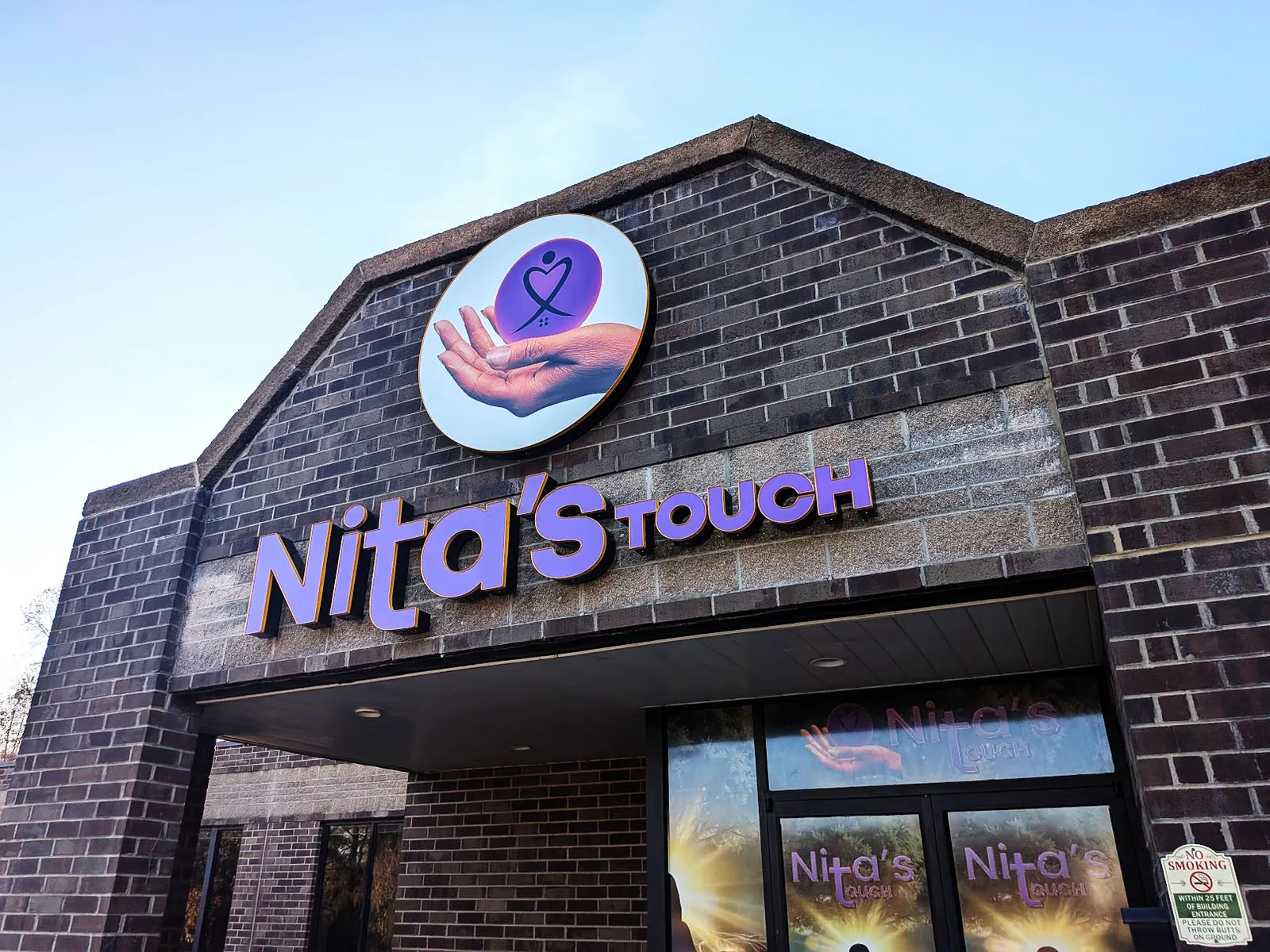 Purple channel letters reading Nita's Touch with a round logo panel installed on a dark brick storefront gable.