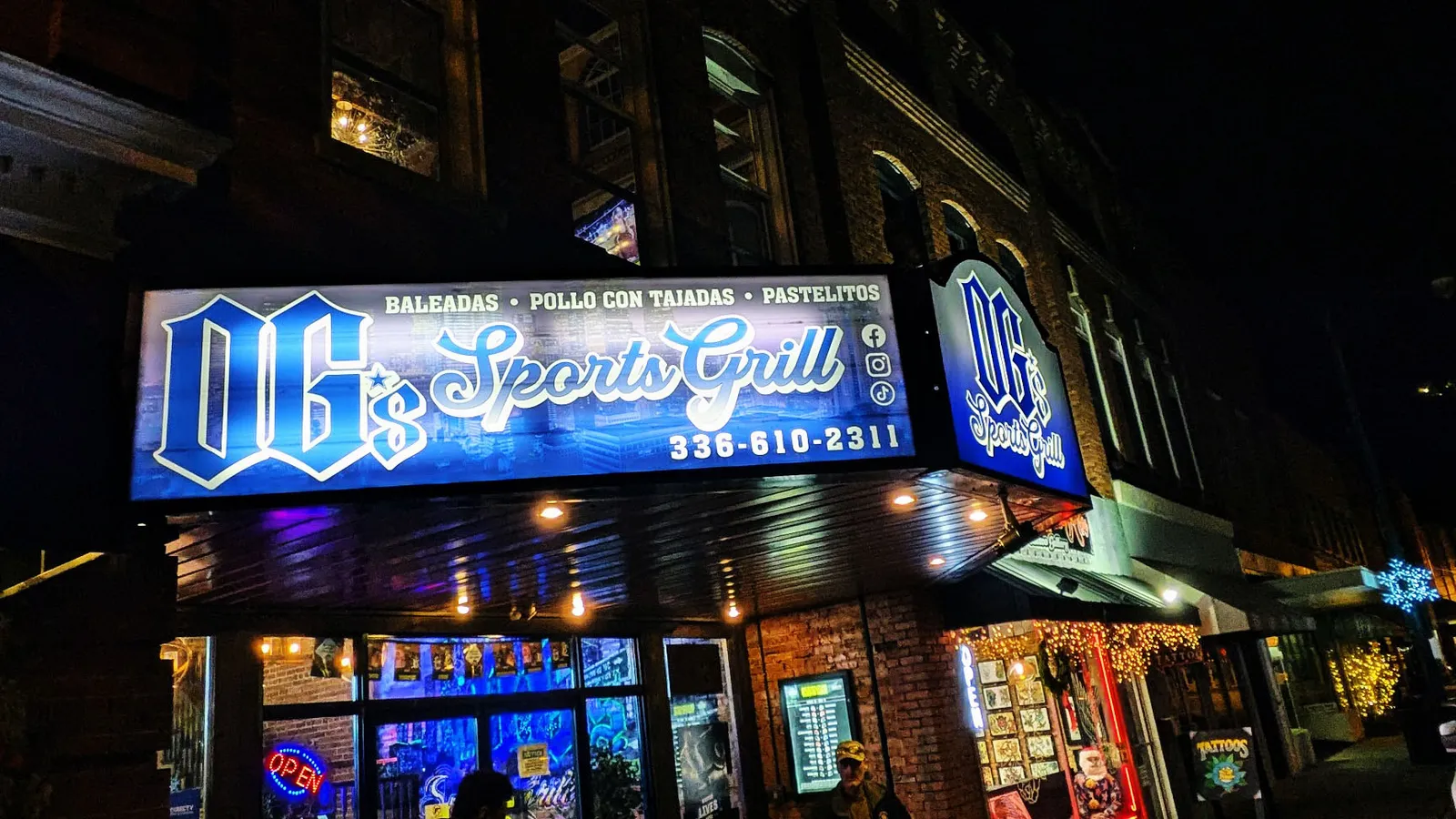 Illuminated blue storefront sign for OG's Sports Grill glowing at night above a downtown restaurant entrance.