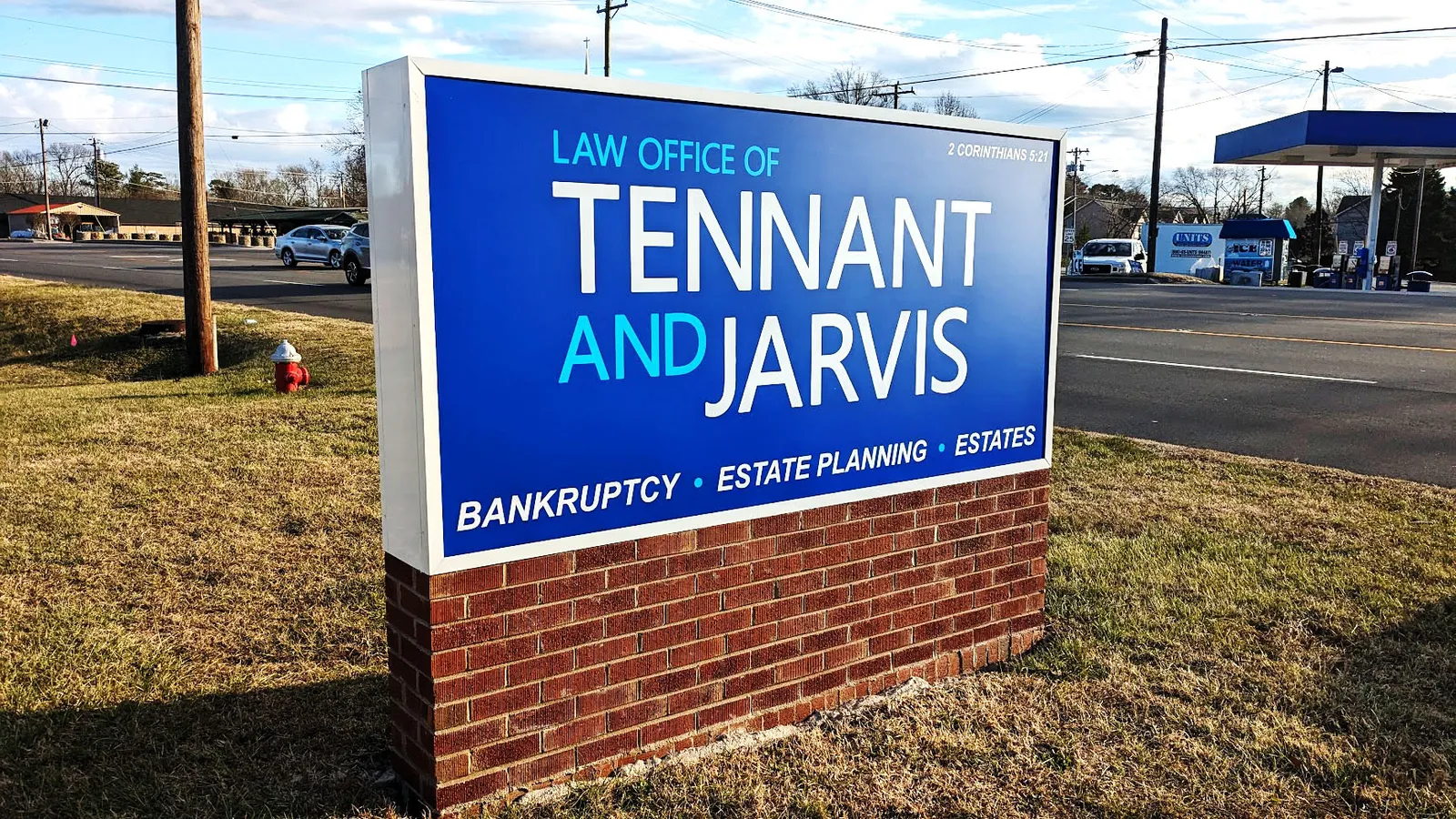 Blue monument sign for the Law Office of Tennant and Jarvis on a brick base beside a roadway.