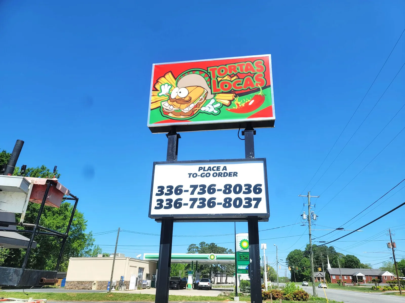Colorful Tortas Locas pylon sign with a cartoon sandwich character and to-go phone numbers against a bright blue sky.