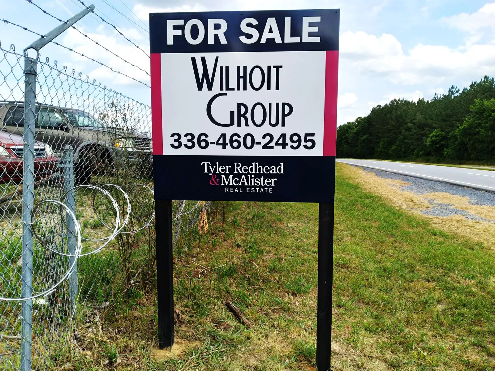For Sale post sign for Wilhoit Group with Tyler Redhead and McAlister Real Estate branding beside a rural road.