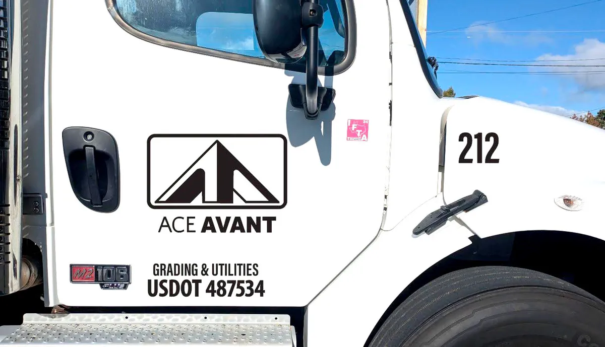 Close-up of a white heavy truck cab door showing the Ace Avant Grading and Utilities logo: a black mountain-peak badge in a rounded rectangle, with Grading and Utilities and USDOT lettering beneath.