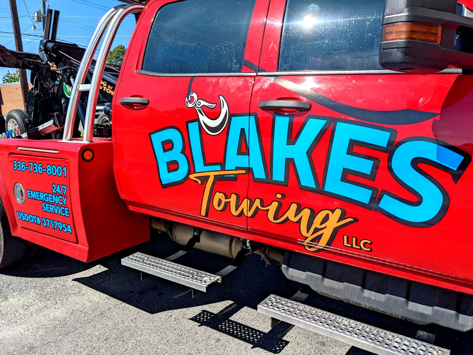 A bright red tow truck with large teal and gold Blake's Towing lettering and a tow hook graphic across the doors.