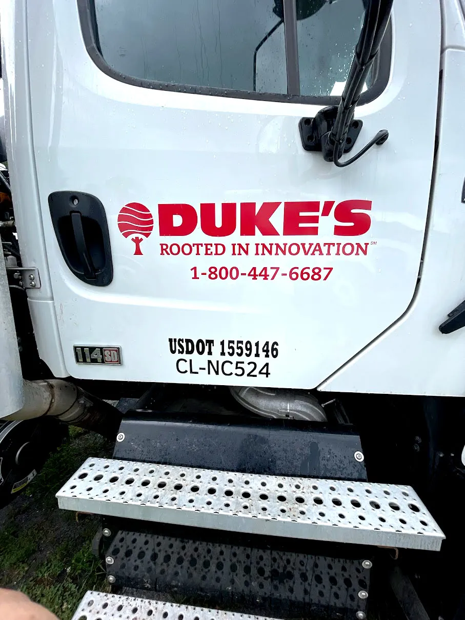 Close-up of a white Freightliner 114SD cab door showing Duke's Rooted in Innovation logo in red with a stylized tree, a toll-free phone number, and USDOT lettering.