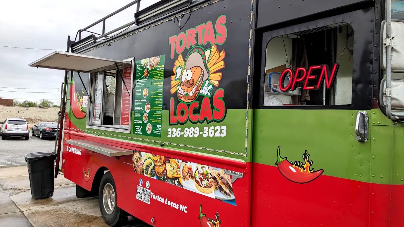 A red, green, and black food truck with Tortas Locas cartoon sandwich artwork, chili pepper graphics, a printed menu, and a neon open sign.